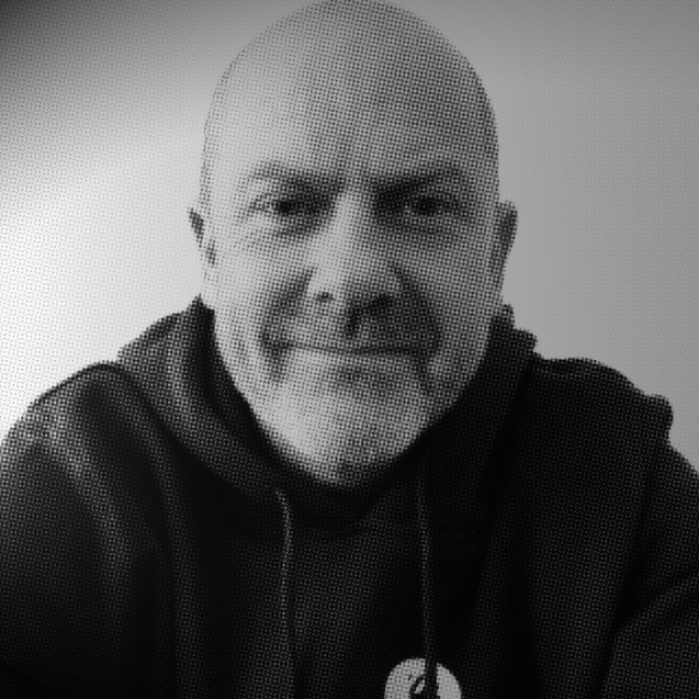 Portrait of a man with brown hair and glasses on a flat gray background.